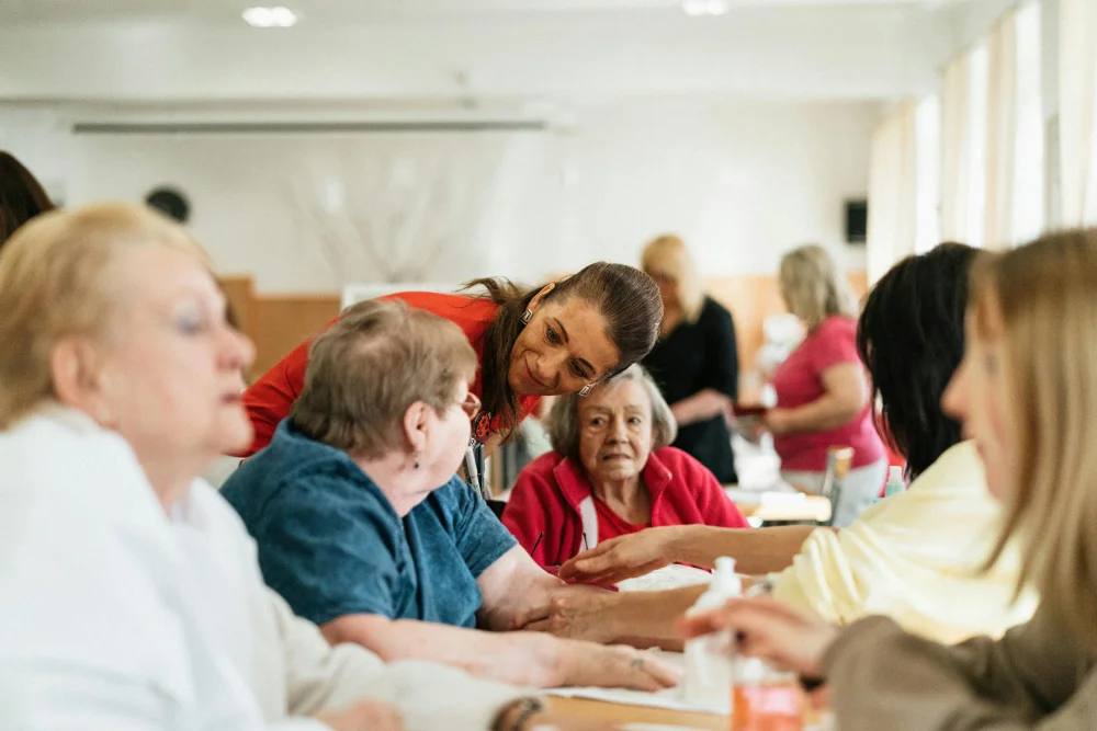 Volunteers at a care facility provide hand massages and personal attention to elderly residents during a wellness and community bonding event.