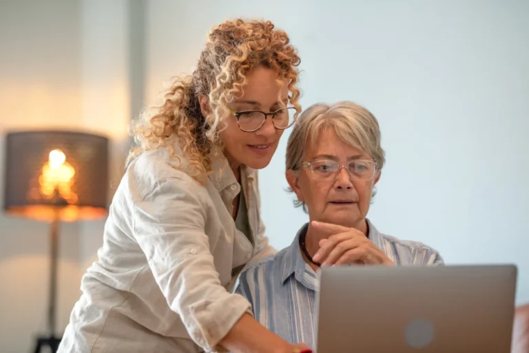 Two women review a laptop together in a bright office.